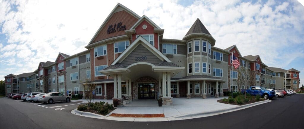 Modern senior living community building showcasing architectural design and Energy Star compliance, featuring multiple stories, large windows, and landscaped entrance with parking area.